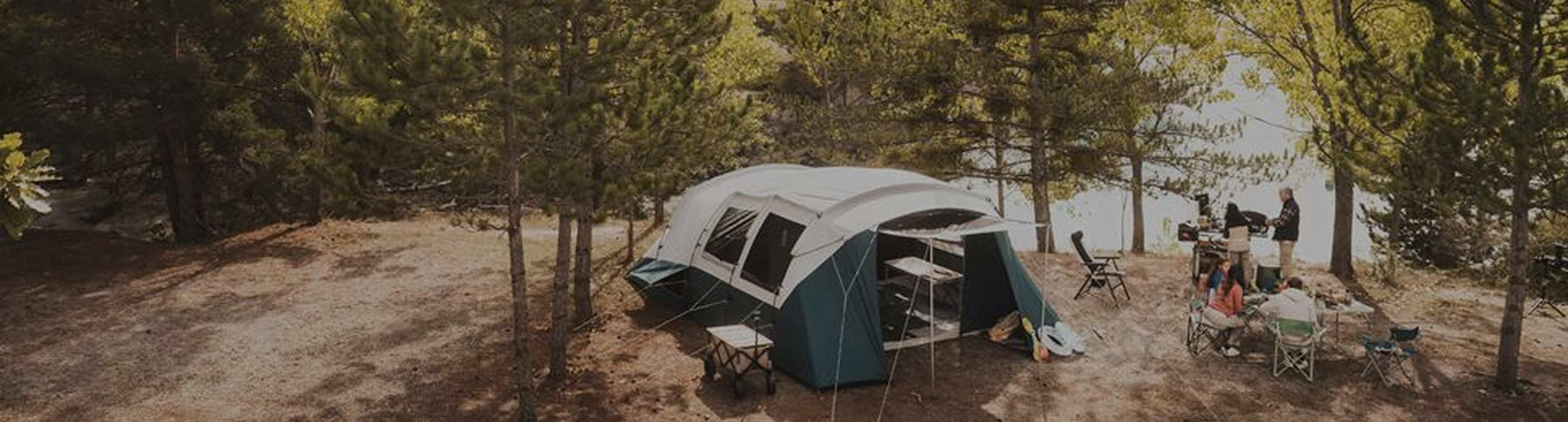 Campamento armado con carpas familiares y mobiliario de camping en un entorno natural boscoso