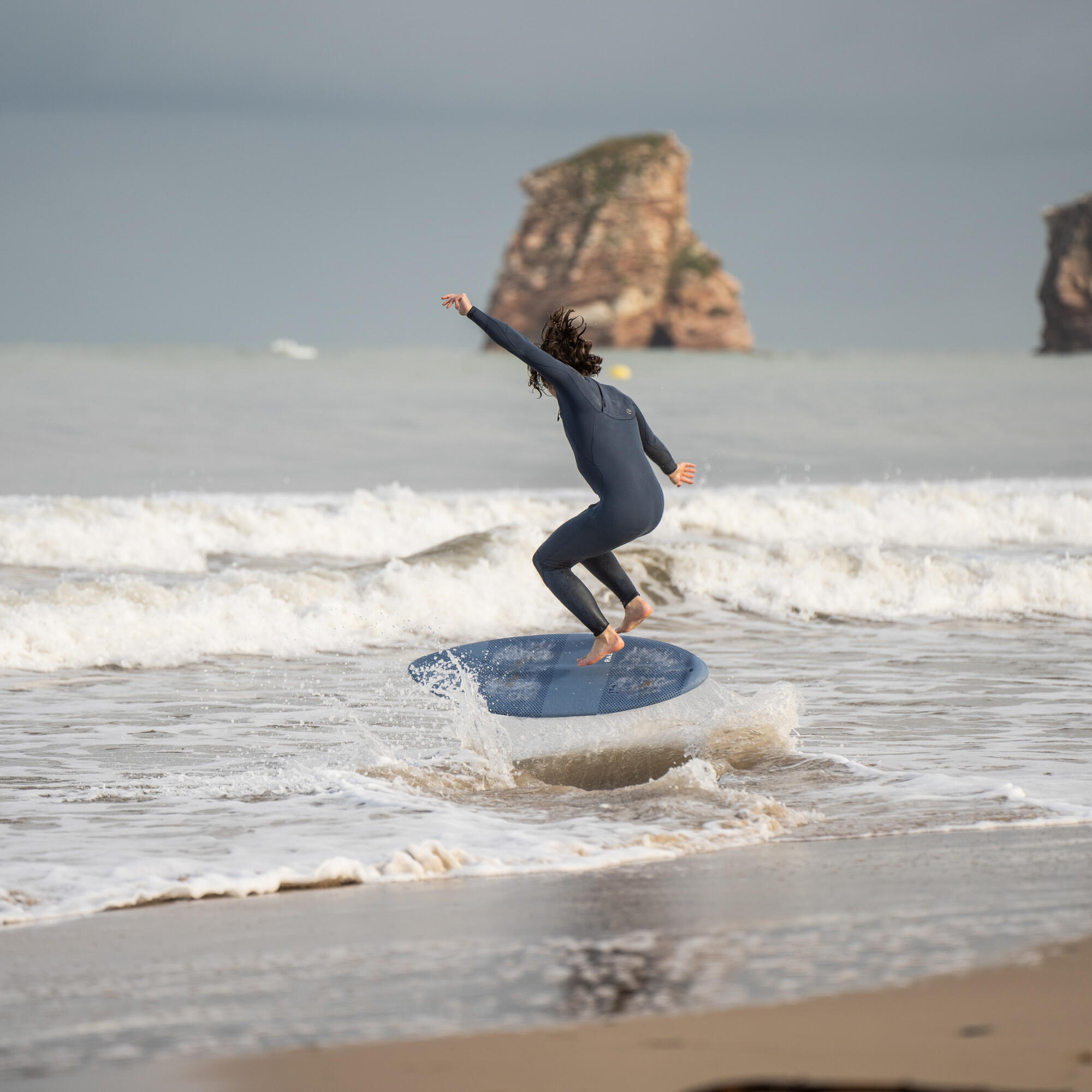 Joven deslizándose en la orilla con una tabla de skimboard sobre una fina capa de agua
